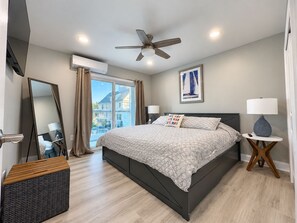 A modern bedroom with a bed, ceiling fan, bedside lamps, and a large window. - Cape May Harbor Getaway with Kayaks & Bikes (Cape May)