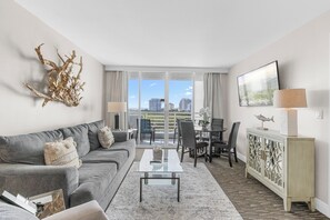 A modern living room with a grey sofa, a glass coffee table, and a dining area with chairs and a table. - 1BR - Intracoastal Views- Steps to Beach (Fort Lauderdale)