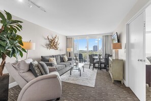 A modern hotel room with a sofa, coffee table, dining area, and a large window with a city view. - 1BR - Intracoastal Views- Steps to Beach (Fort Lauderdale)
