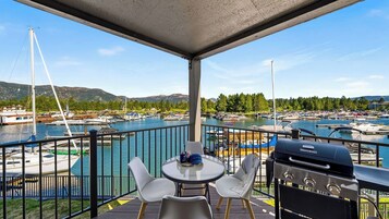 Un balcón con mesa y sillas, con vistas a un puerto deportivo con barcos y montañas al fondo.