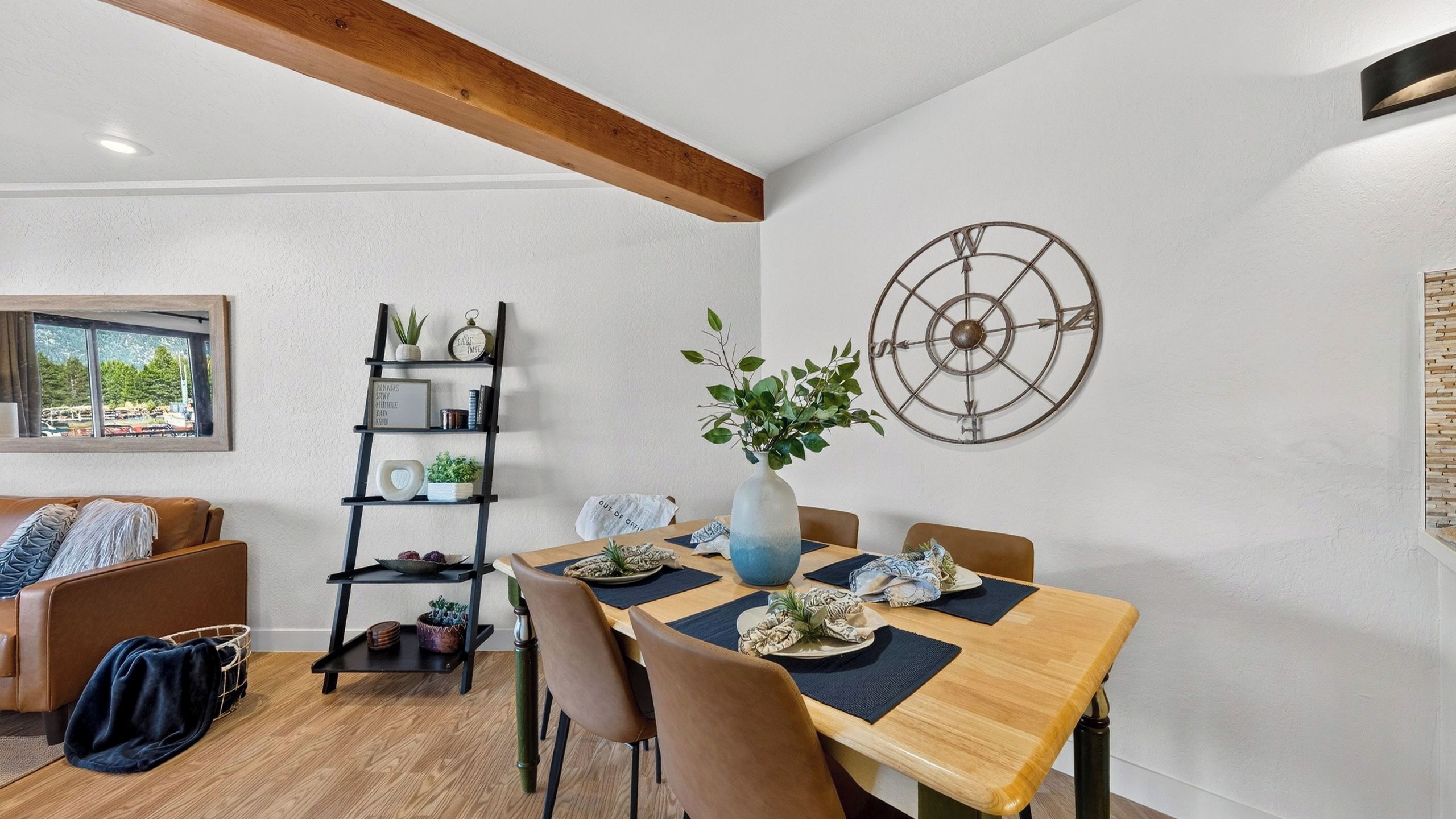 A dining area with a wooden table, chairs, a decorative wall clock, and a plant centerpiece.