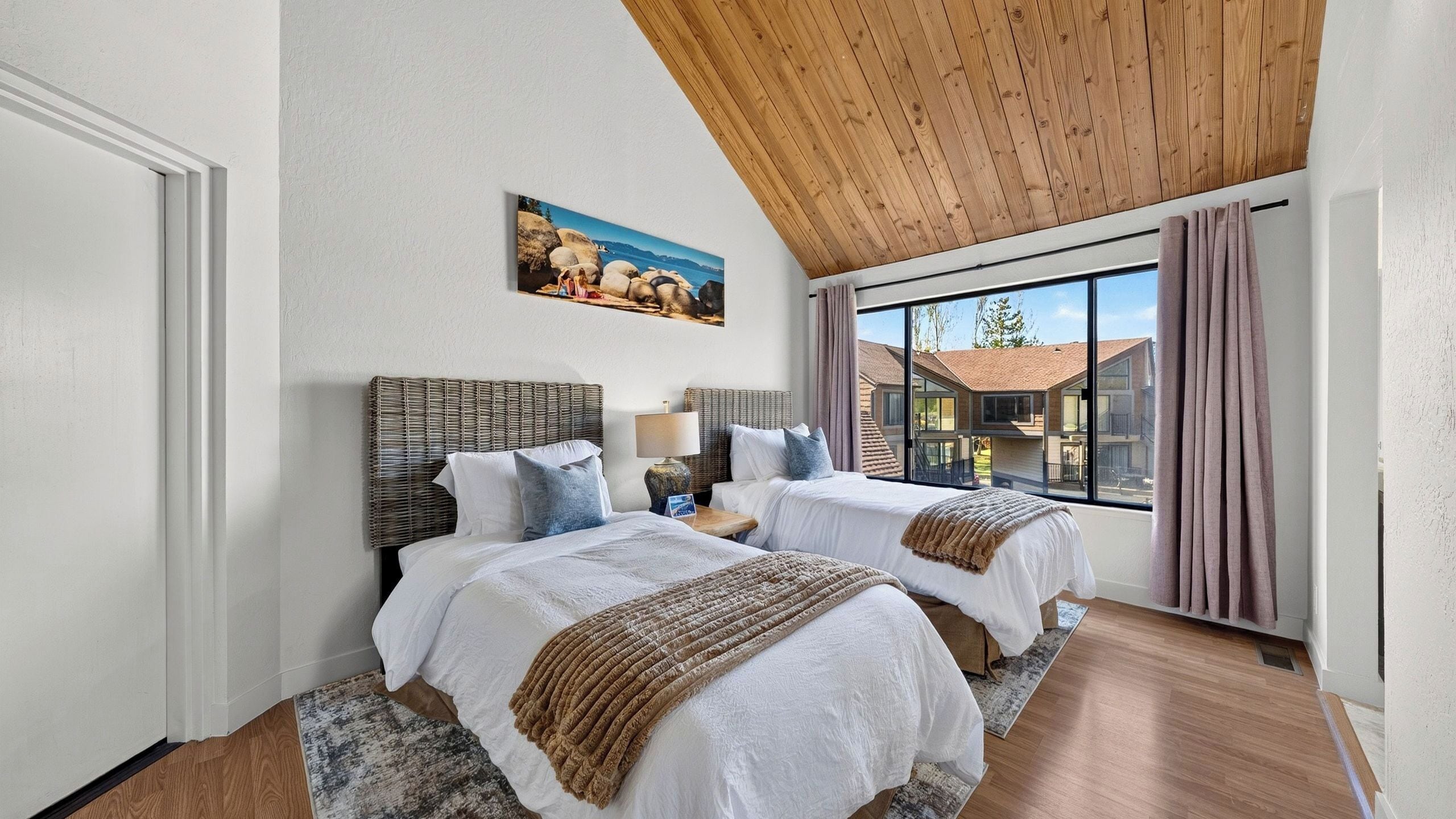 Une chambre avec deux lits, un plafond en bois, un tableau et une vue sur des immeubles.