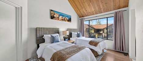 Un dormitorio con dos camas, techo de madera, un cuadro y vistas a edificios.