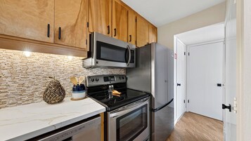 Una cocina con armarios de madera, microondas, refrigerador, horno y encimera de mármol.