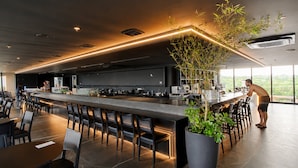A modern bar area with a long counter, seating, and a large potted plant. - Hosts BR - Studio GAV Resorts (Ipojuca)
