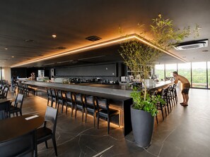 A modern bar area with a long counter, seating, and a large potted plant. - Hosts BR - Studio GAV Resorts (Ipojuca)