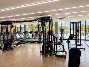 A gym with treadmills, weight machines, and a view of a pool and palm trees. - Hosts BR - Studio GAV Resorts (Ipojuca)