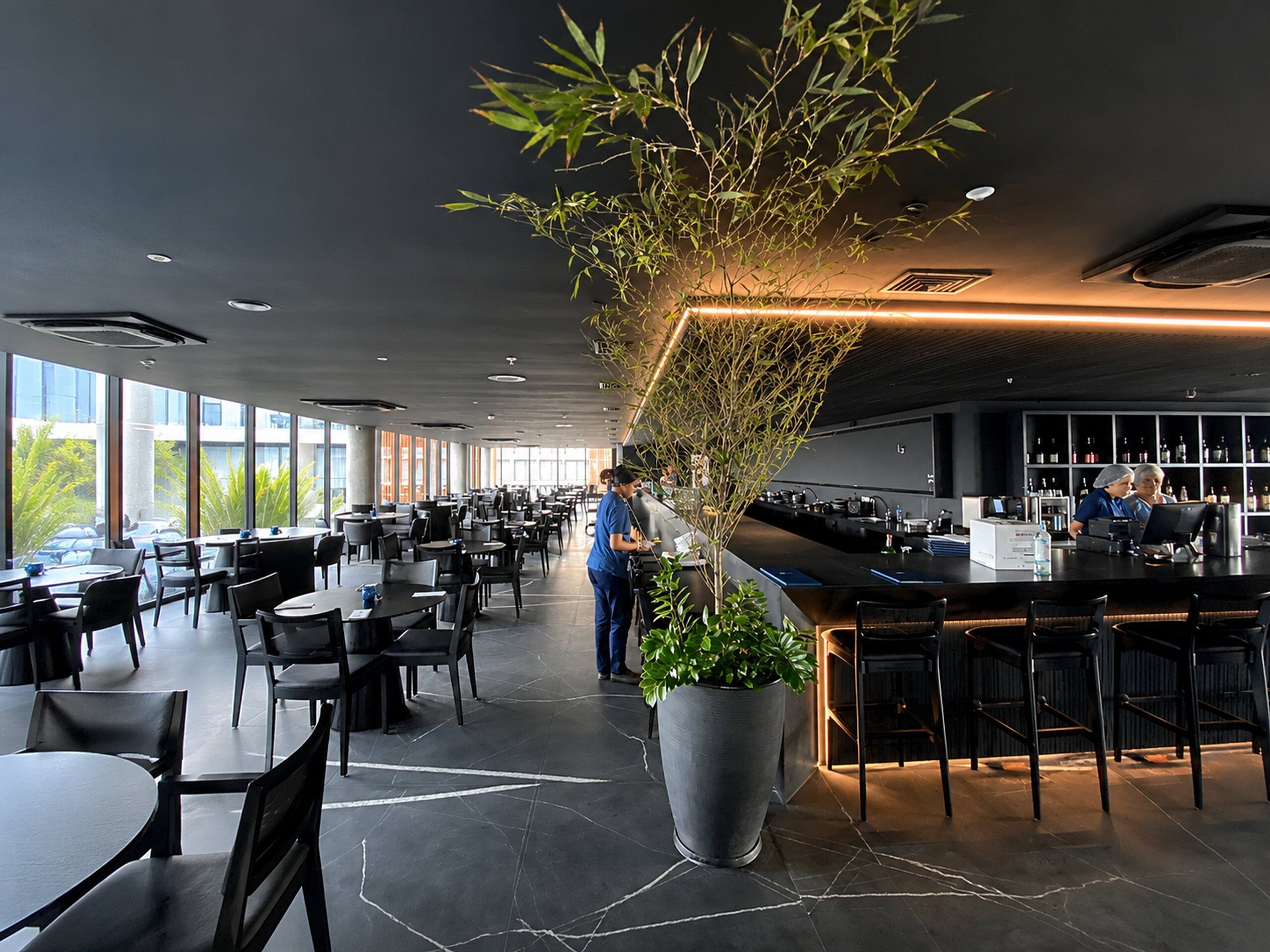 Um restaurante moderno com um balcão comprido, grandes vasos de plantas e um espaço de bar.