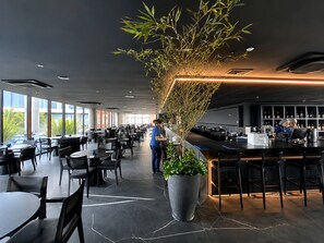 Um restaurante moderno com um balcão comprido, grandes vasos de plantas e um espaço de bar.