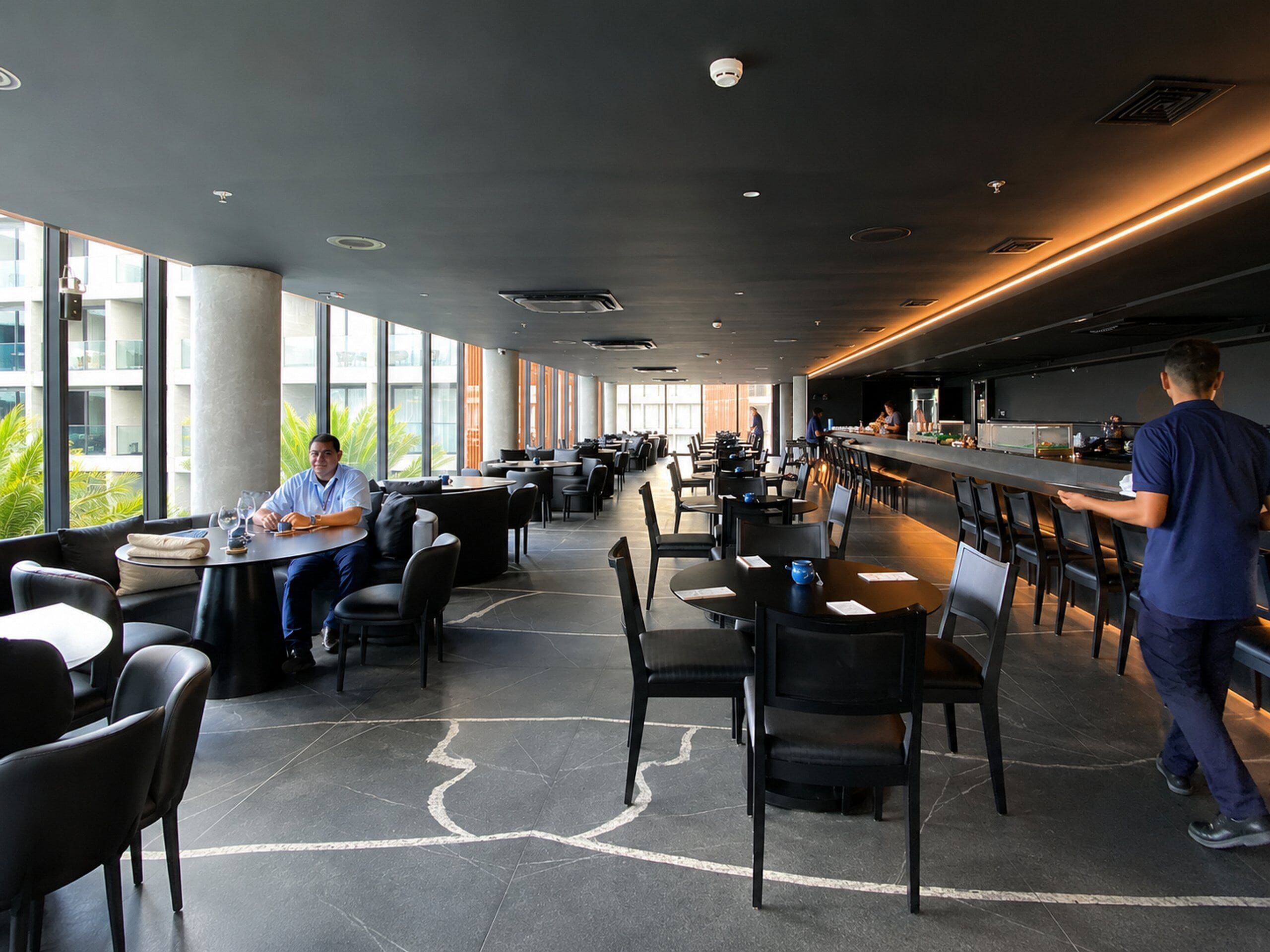 A modern restaurant with high ceilings, large windows, and a bar area.