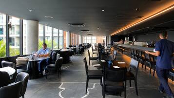 A modern restaurant with high ceilings, large windows, and a bar area.