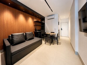 Um interior moderno com um sofá de couro preto, uma área de jantar com mesa redonda e cadeiras, e um aparelho de ar condicionado na parede.