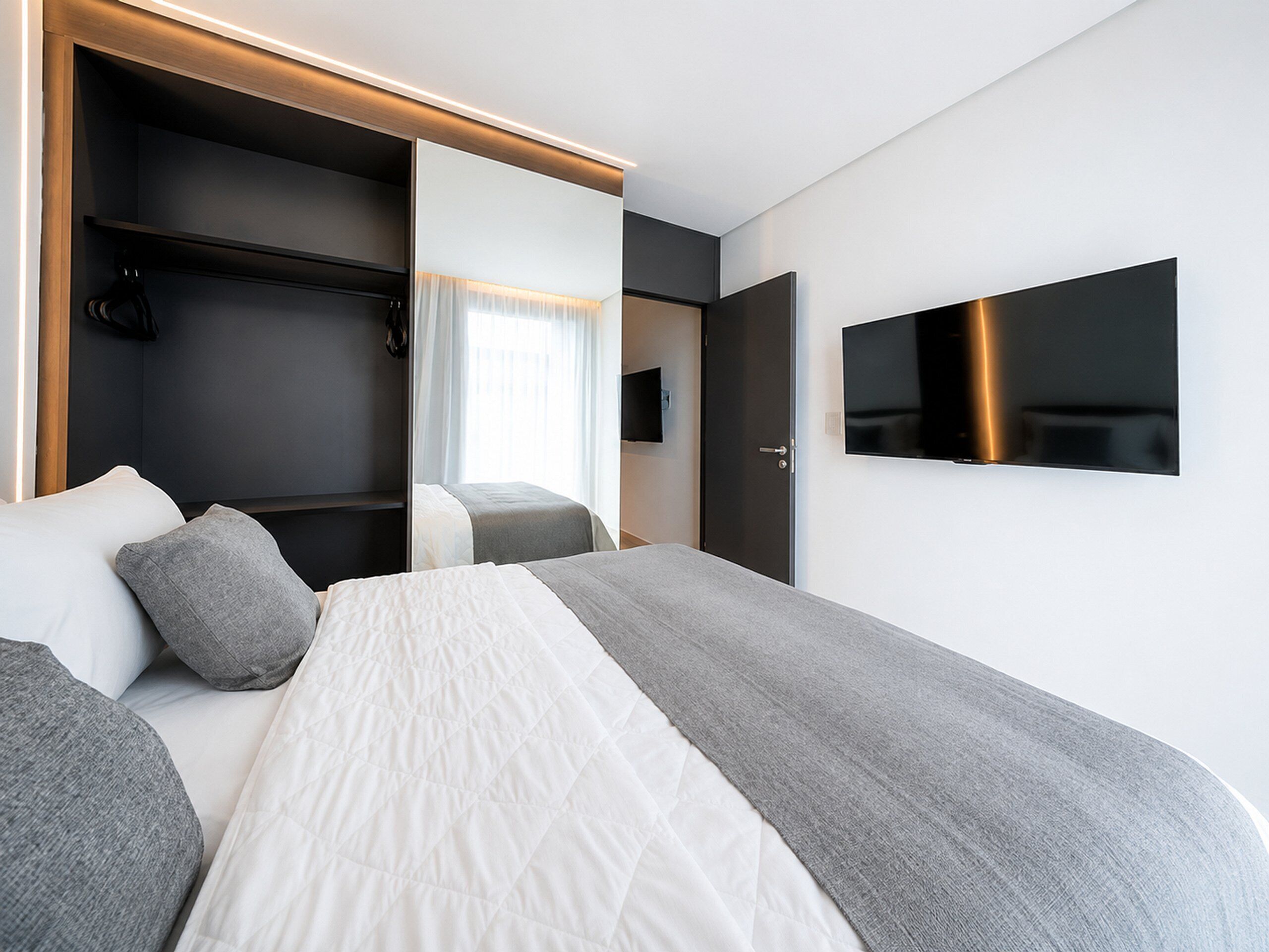 A modern hotel room with a bed, a TV, and a wardrobe.