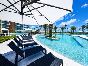 Ein Hotelpoolbereich mit Liegestühlen, Sonnenschirmen und blauem Himmel.