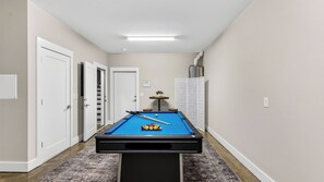 Ein Billardtisch in einer Diele mit Türen an beiden Seiten, ein kleiner Tisch mit einer Pflanze und ein weißes Schranksystem.