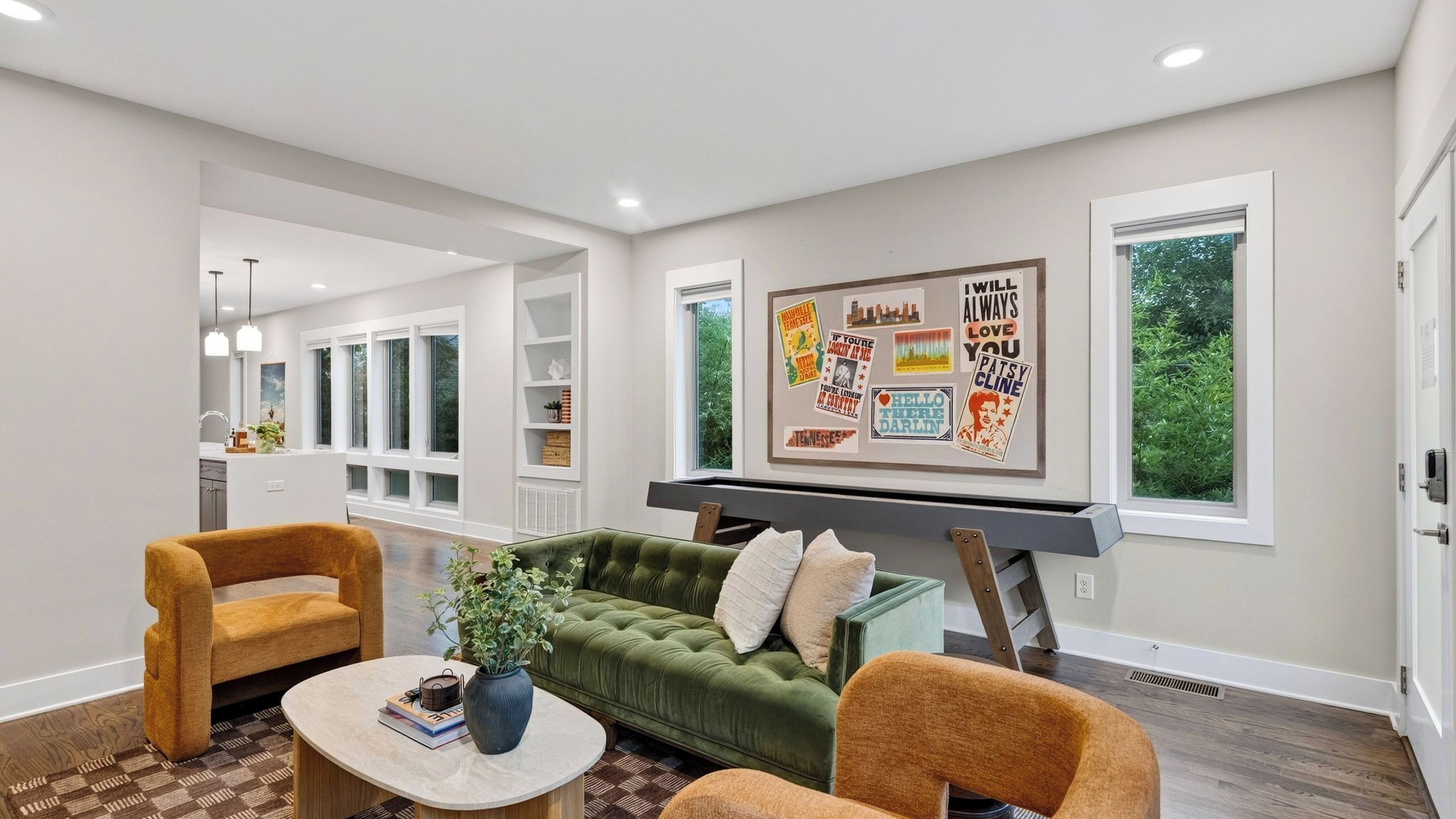 A living room with a green sofa, two armchairs, a coffee table, and a wall with various framed posters.
