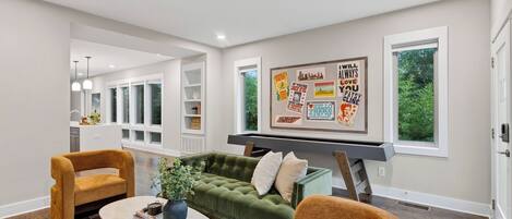 A living room with a green sofa, two armchairs, a coffee table, and a wall with various framed posters.