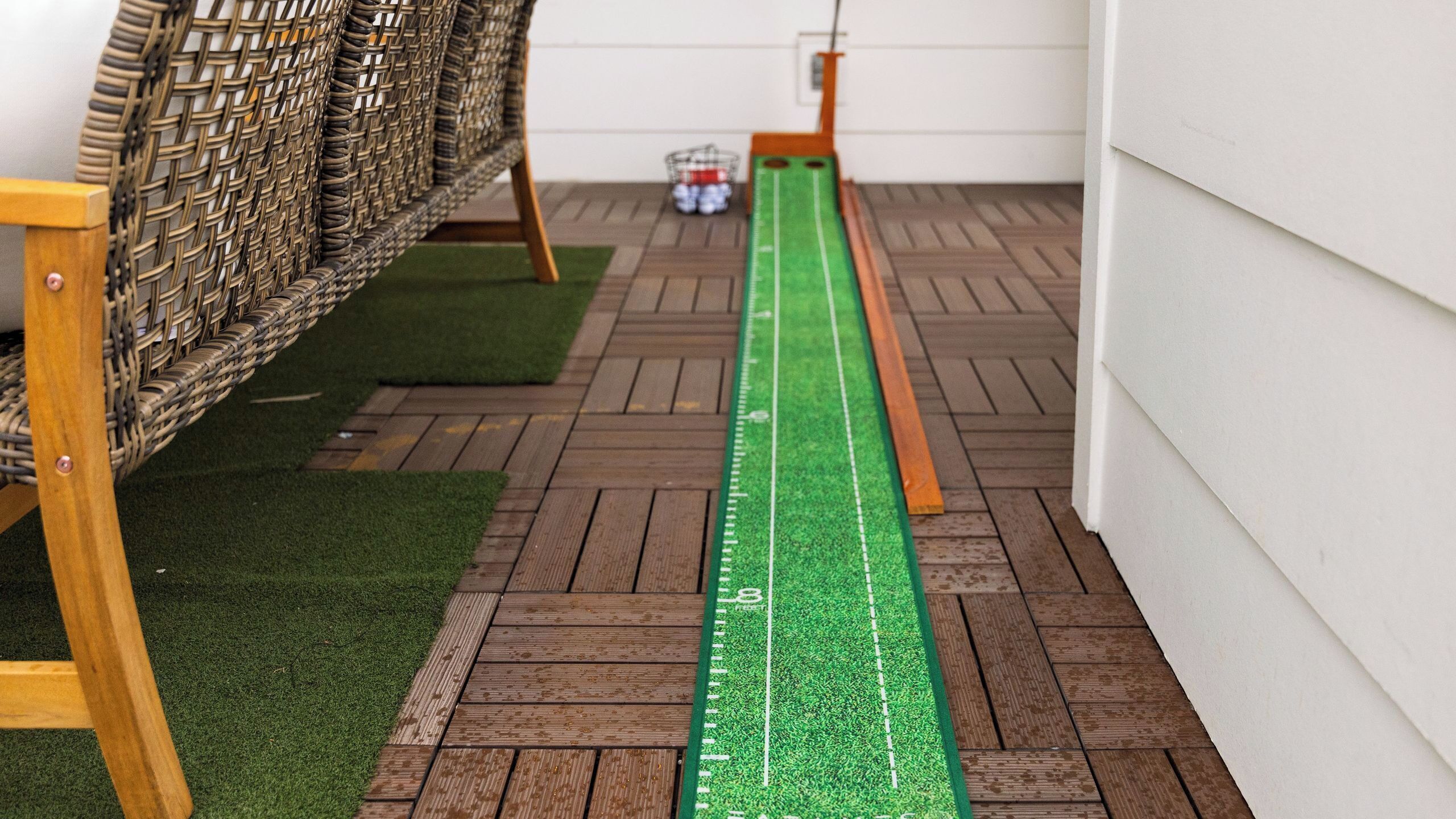 Una terraza de madera con área de césped artificial verde, un metro y una silla de mimbre.