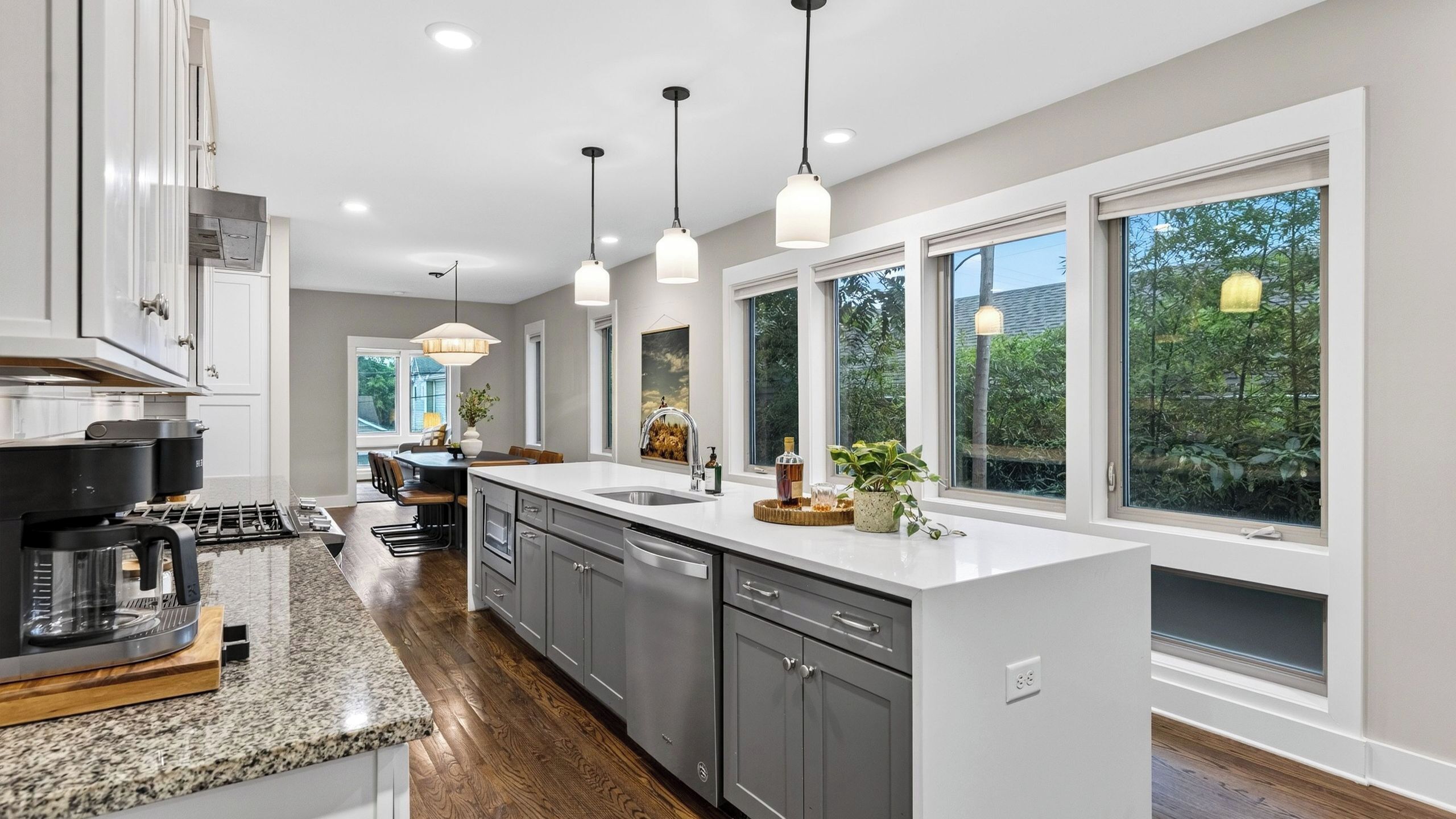 A modern kitchen with a central island, pendant lighting, and large windows.
