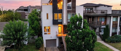 A modern multi-story residential building with a garage, a balcony, and a well-maintained lawn.
