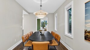 A dining room with a round table, six chairs, a hanging light fixture, and a window with a view of trees. - The Mod Buchanan by Avantstay Hot Tub + Rooftop Putting Mat + Game Room (Nashville)