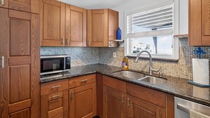 A kitchen with wooden cabinets, a microwave, a sink, and a window with blinds. - Beach views, steps to the sand, & pet friendly! (Galveston)