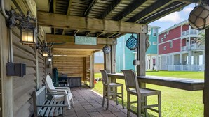 A covered patio with wooden chairs and a table, a grill, and a sign pointing to the beach. - Beach views, steps to the sand, & pet friendly! (Galveston)