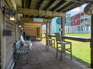 Eine überdachte Terrasse mit Holzsesseln, einem Tisch, einem Grill und einem Schild, das zum Strand weist.