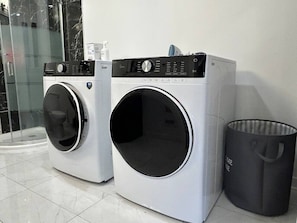 Two front-loading washing machines and a trash can in a laundry room. - Stylish 4-Bedroom Home (Gatineau)