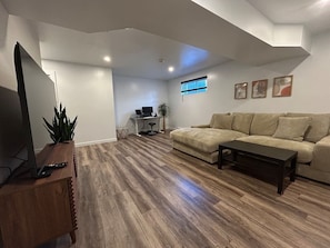 A living room with a sofa, coffee table, TV, and a desk with a computer. - Stylish 4-Bedroom Home (Gatineau)
