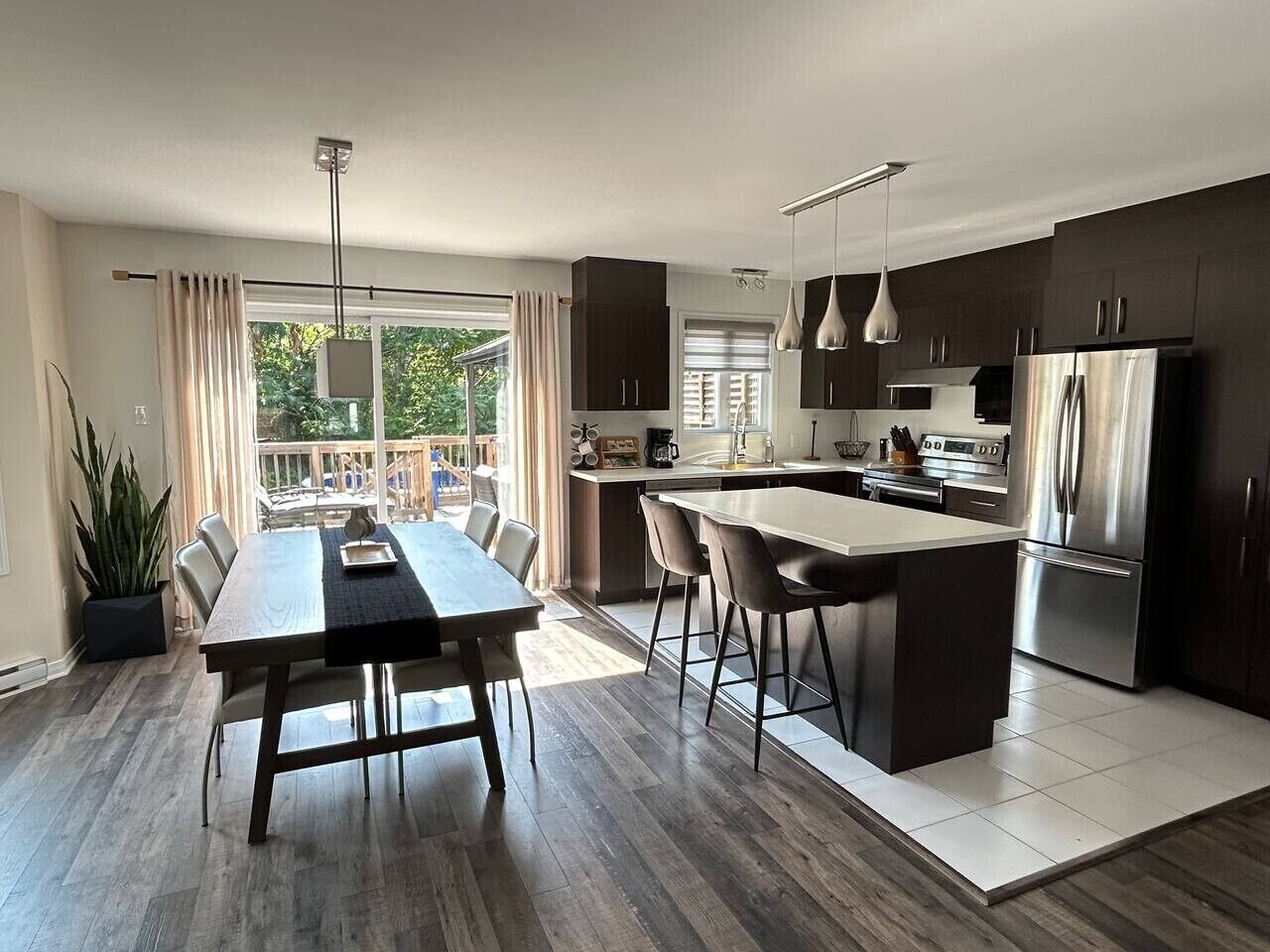 A modern kitchen with a central island, dark cabinetry, and stainless steel appliances.