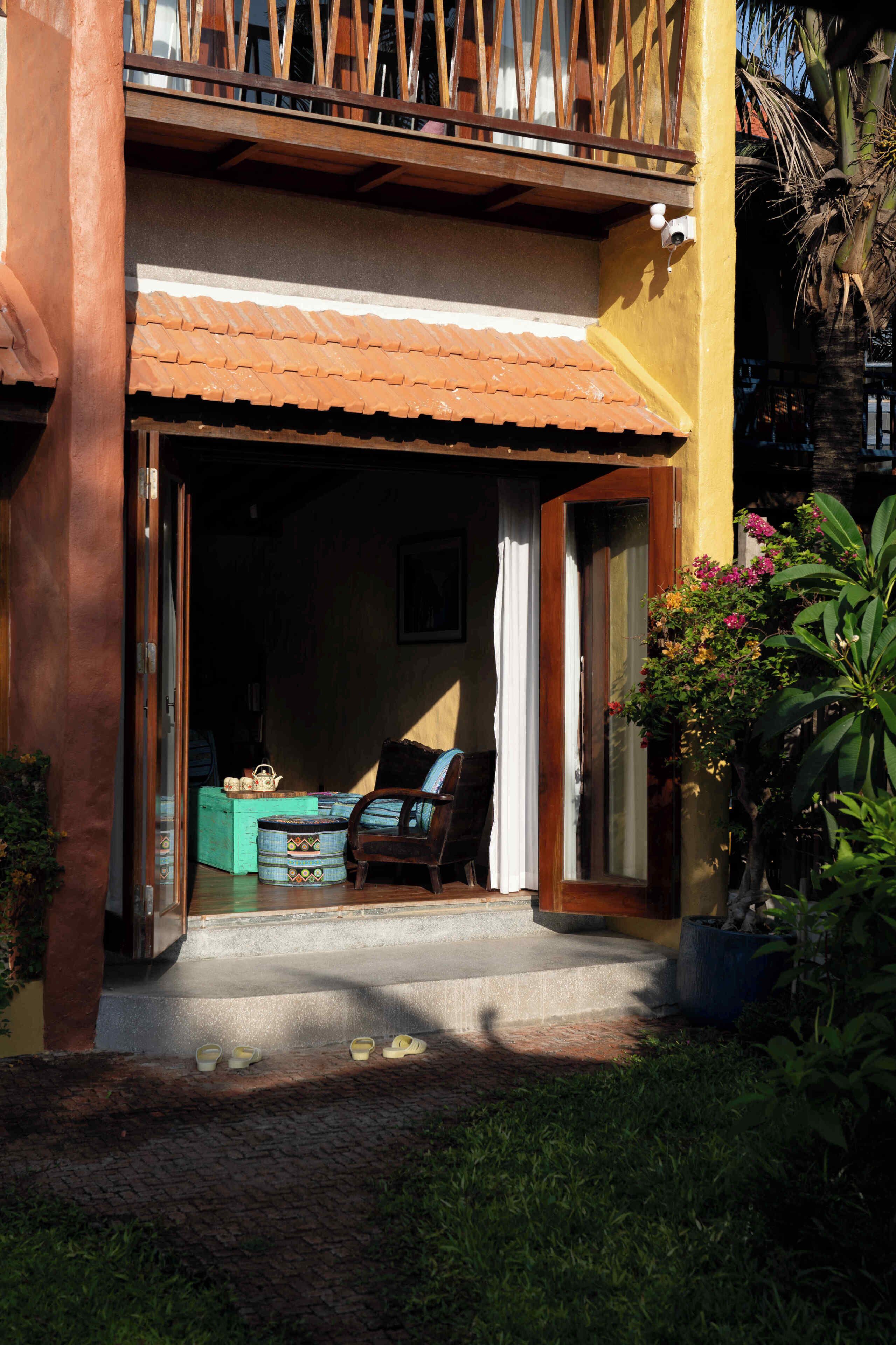 A building entrance with a tiled roof, a wooden chair, a table with a teapot, and a potted plant.