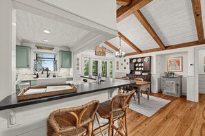 A spacious kitchen with a large island, wooden beams, and a view to the outdoors. - Mtn-View Cashiers Cottage w Screened Deck! (Glenville)
