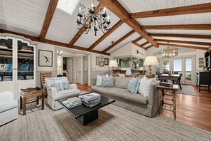 A spacious living room with a high ceiling, exposed wooden beams, a fireplace, and a dining area with a view. - Mtn-View Cashiers Cottage w Screened Deck! (Glenville)