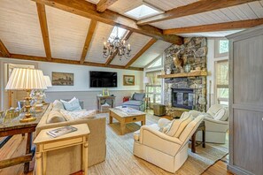 A spacious living room with a stone fireplace, wooden beams, a chandelier, and comfortable seating. - Mtn-View Cashiers Cottage w Screened Deck! (Glenville)