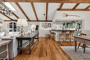 A spacious room with wooden beams, a dining area with rattan chairs, and a kitchen with green cabinets. - Mtn-View Cashiers Cottage w Screened Deck! (Glenville)