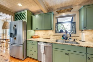 A kitchen with green cabinets, a stainless steel refrigerator, a granite countertop, and a window with a view. - Mtn-View Cashiers Cottage w Screened Deck! (Glenville)