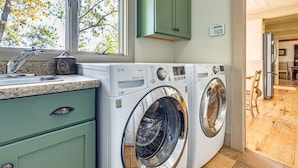 A laundry area with two front-loading washing machines, a sink, and a window with a view of trees. - Mtn-View Cashiers Cottage w Screened Deck! (Glenville)