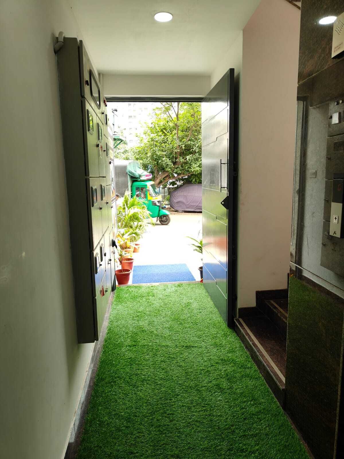 A hallway with artificial grass, potted plants, and a green vehicle outside.