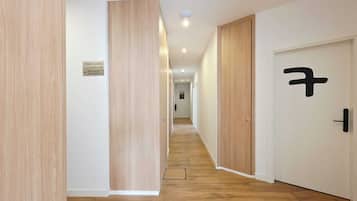 Un pasillo con piso de madera, paredes blancas y puertas con manijas negras. Un cartel indica la disponibilidad de habitaciones.