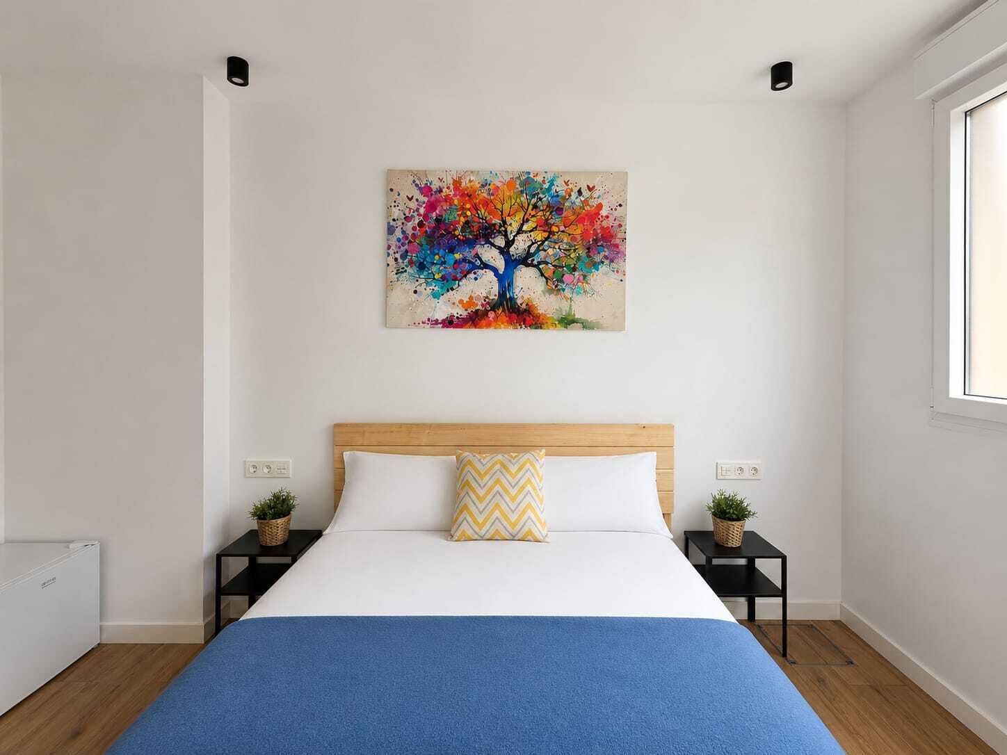 A bedroom with a bed, a colorful abstract painting above the bed, and two bedside tables with small plants.
