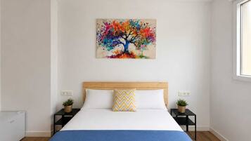 Un dormitorio con una cama, un cuadro abstracto colorido sobre la cama y dos mesitas de noche con plantas pequeñas.