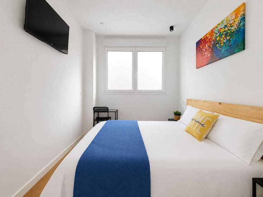 Une chambre à coucher avec un lit, un téléviseur fixé au mur, une fenêtre et un tableau.