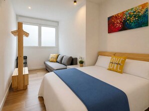 Un dormitorio con una cama, un sofá, una silla de madera, una mesita y un cuadro en la pared.