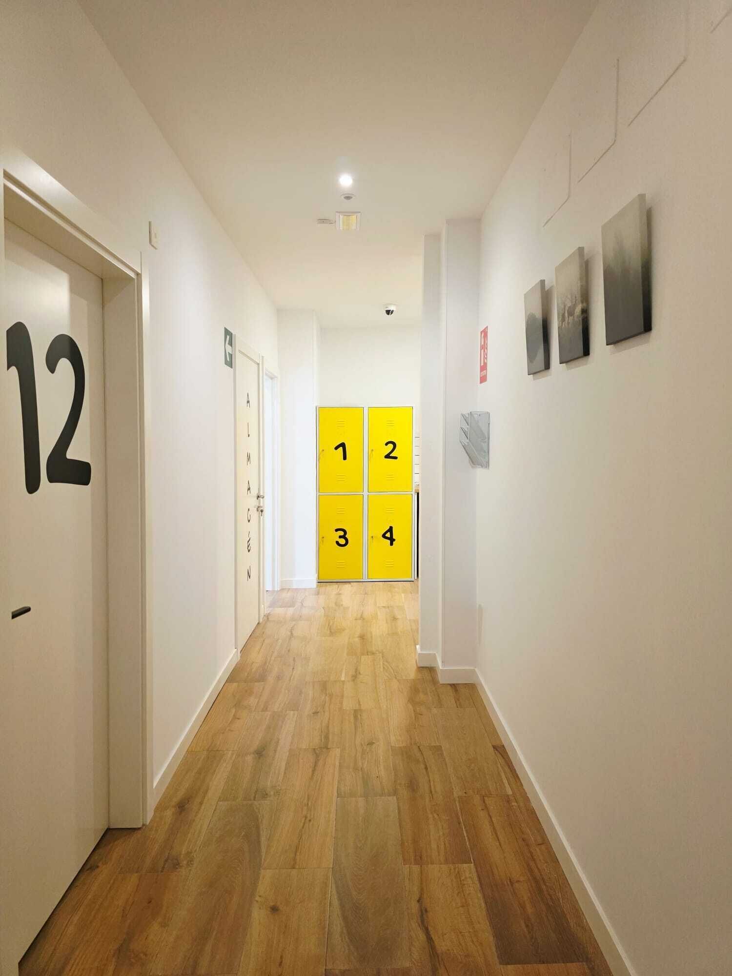 Un pasillo con puertas numeradas, un detector de incendios y un extintor de pared.
