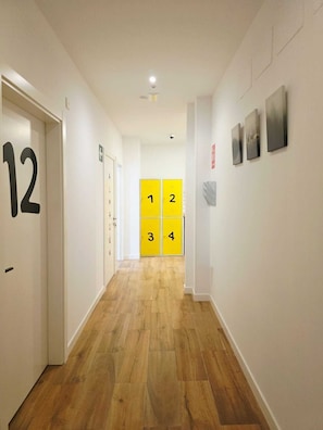 A hallway with numbered doors, a fire alarm, and a wall-mounted fire extinguisher. - Bilbao ROOMS & KITCHEN Zurbaran (Bilbao)