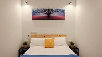 Un dormitorio con una cama, un cuadro en la pared y dos mesitas de noche con lámparas.