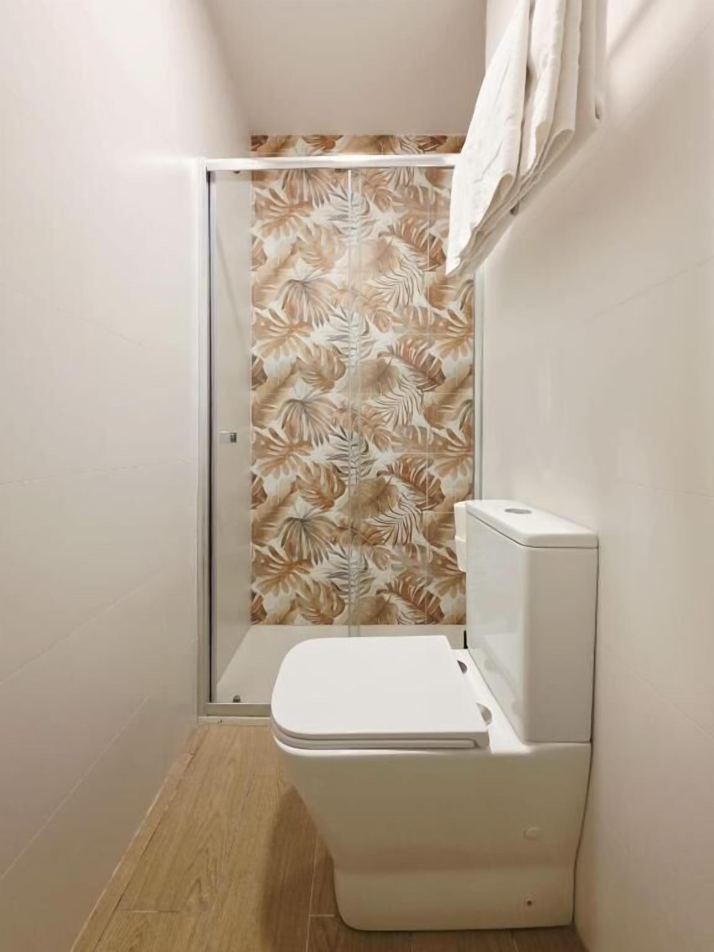 Een compacte badkamer met toilet, douche en een muur met bladmotief.