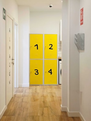Un pasillo con cuatro taquillas numeradas, un letrero de salida de incendios y un detector de incendios en la pared.