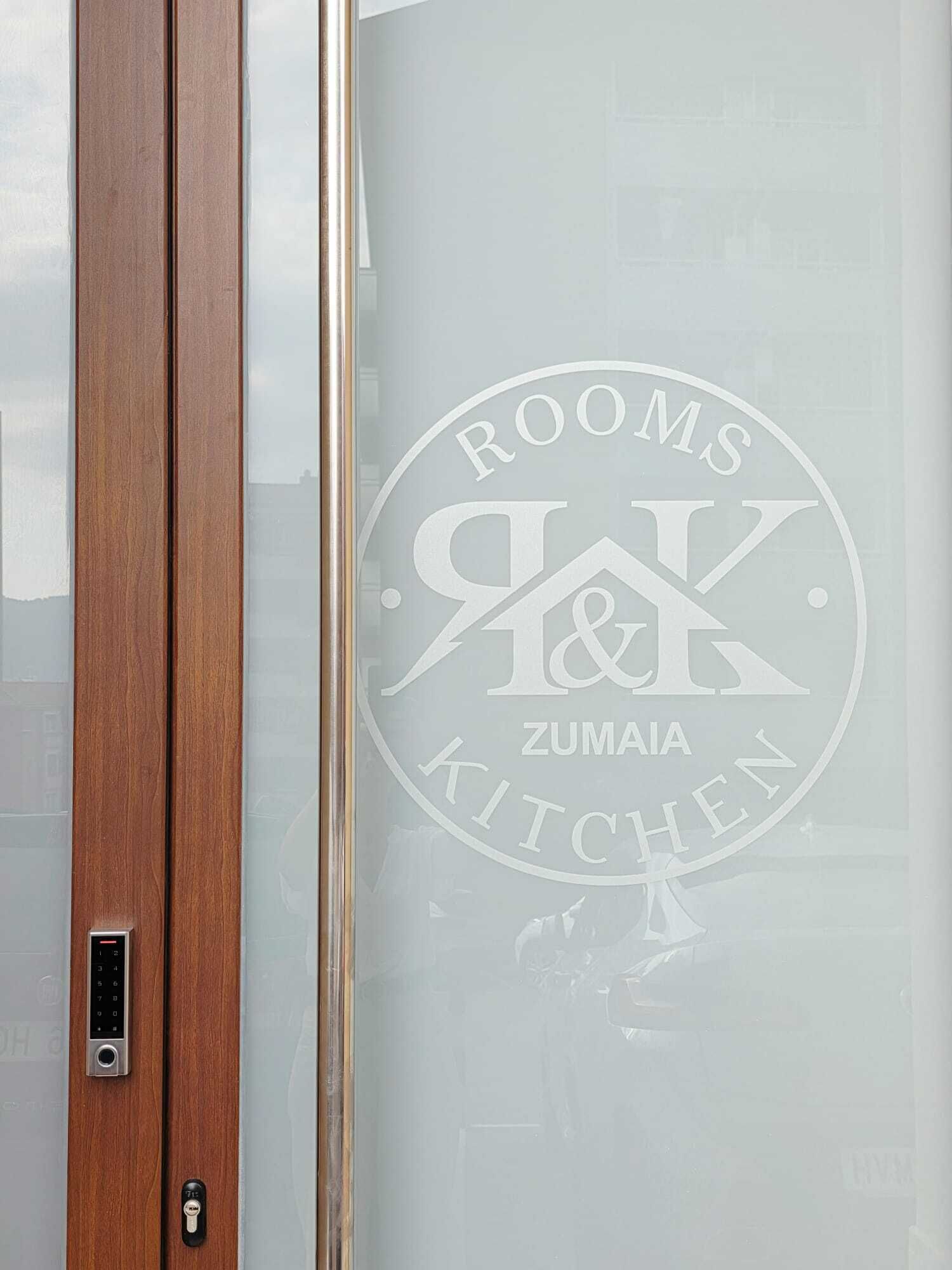 Una puerta de vidrio empañada con un logotipo y texto que indica 'ROOMS & KITCHEN' y 'ZUMAIA'.